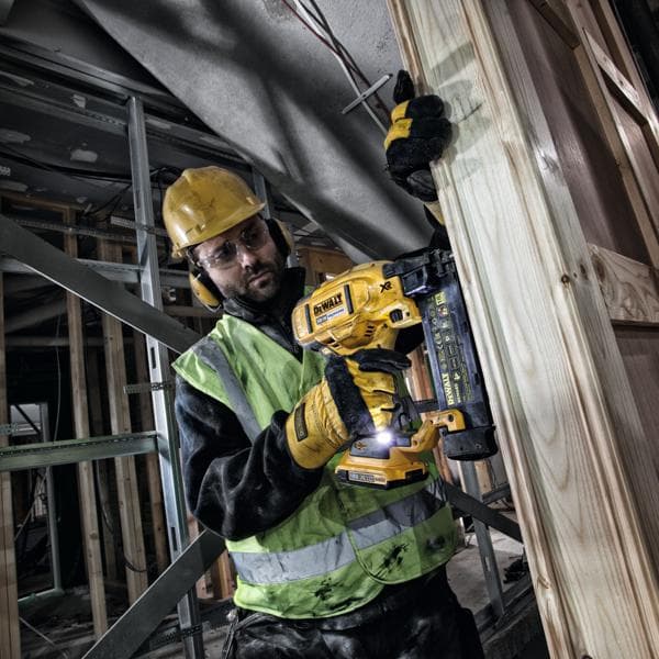 Trabajador usa clavadora DEWALT DCN680 en marco de madera, equipado con ropa de seguridad.