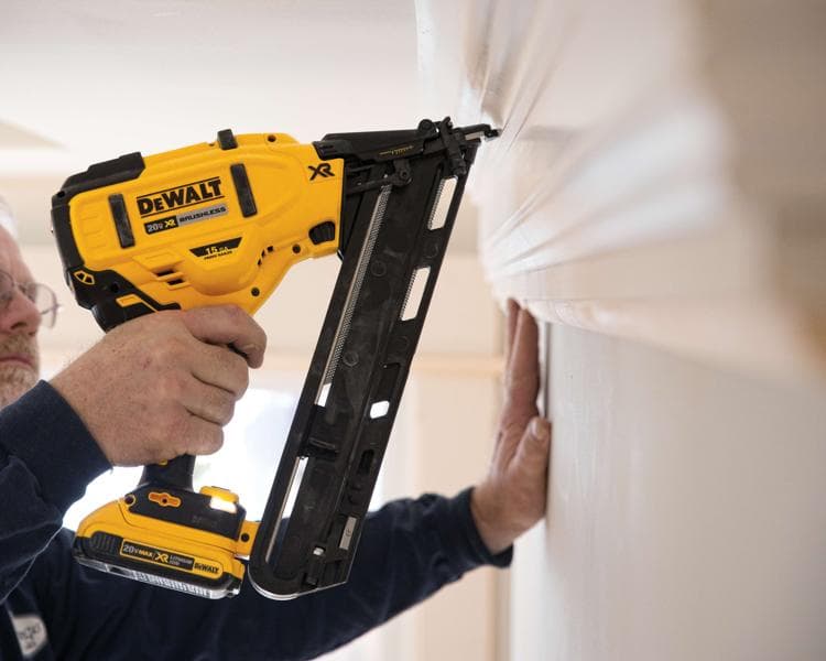 Una persona usando una pistola de clavos inalámbrica DEWALT 20V XR sin escobillas para fijar molduras en una pared.