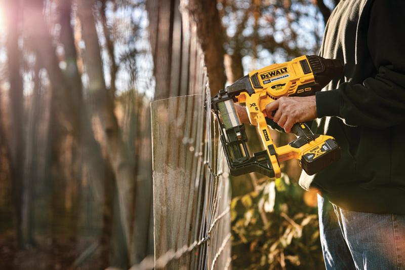 Una persona usando una grapadora inalámbrica para cercas DEWALT para asegurar una cerca de alambre al aire libre, con árboles y luz solar en el fondo.