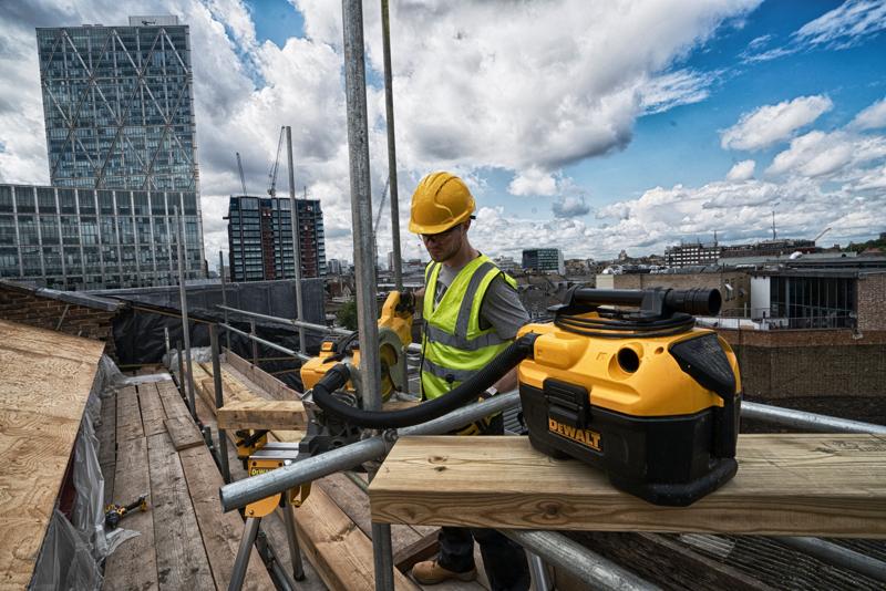 Aspiradora DEWALT DCV584 en obra en la azotea con trabajador y edificios urbanos al fondo.