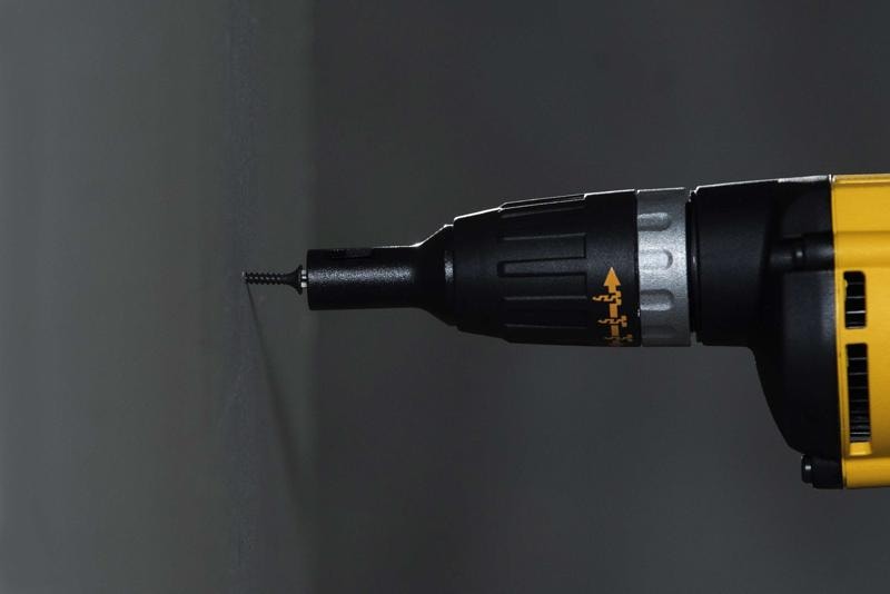 Imagen en primer plano de una herramienta eléctrica DEWALT amarilla y negra, específicamente un destornillador, atornillando un tornillo en una pared.