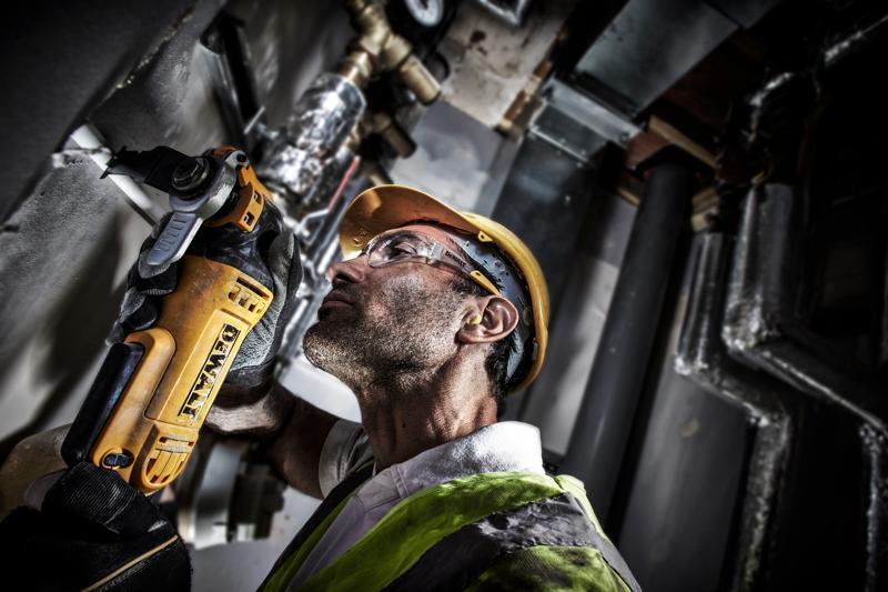 Trabajador corta tubo con DEWALT DWE315, lleva casco y chaleco en entorno industrial.