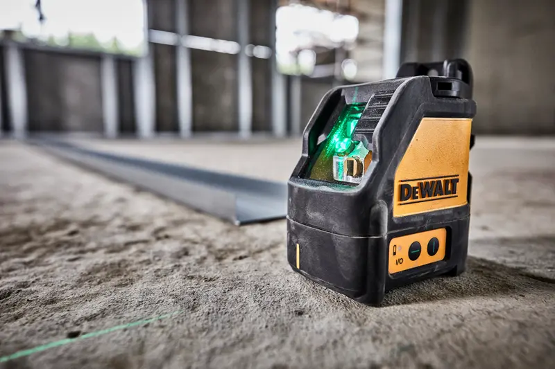 Foto del nivel láser verde DEWALT DW088CG en suelo de obra, proyectando línea. Herramienta fotográfica.